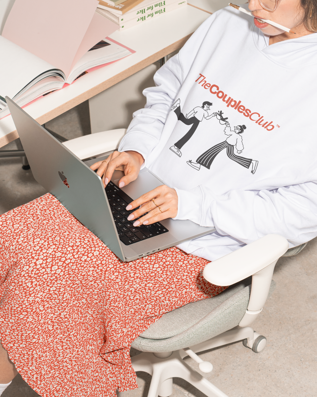 Person using a laptop while wearing a 'The Couples Club' hoodie in a casual setting.