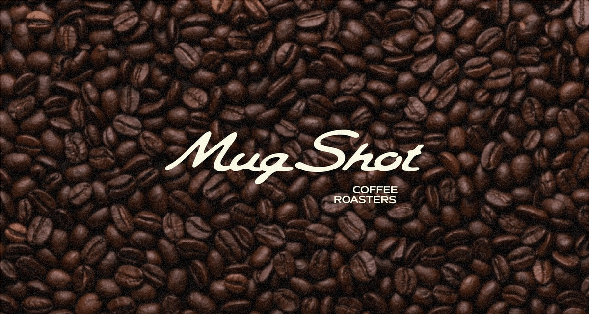 Mug Shot Coffee Roasters script wordmark in cream over a full bed of roasted coffee beans