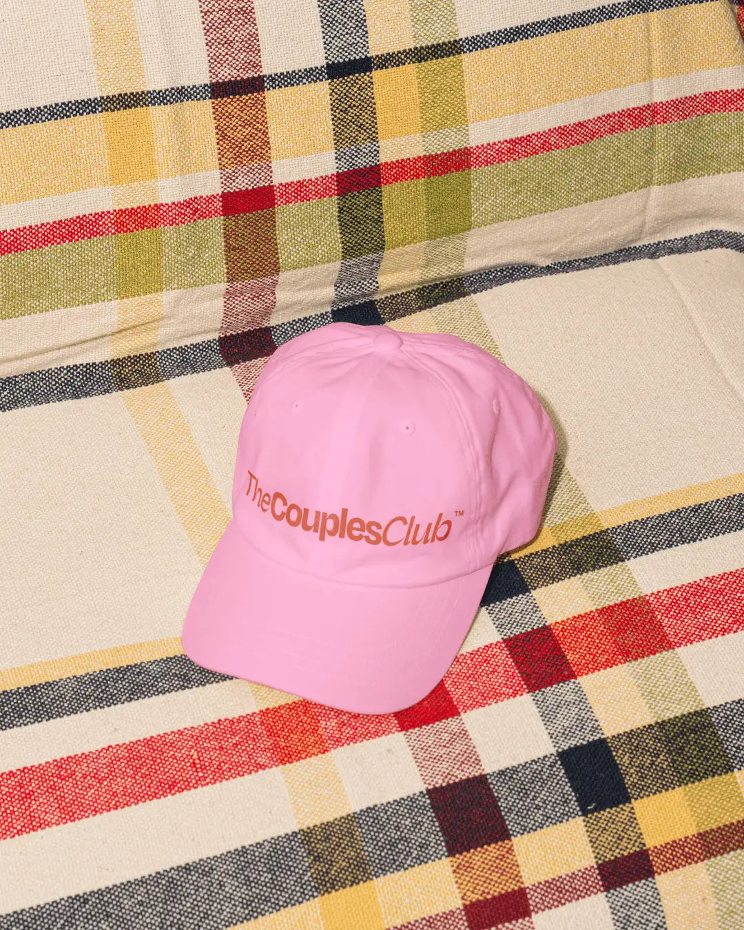 The Couples Club merch design: pink dad cap with embroidered red wordmark logo