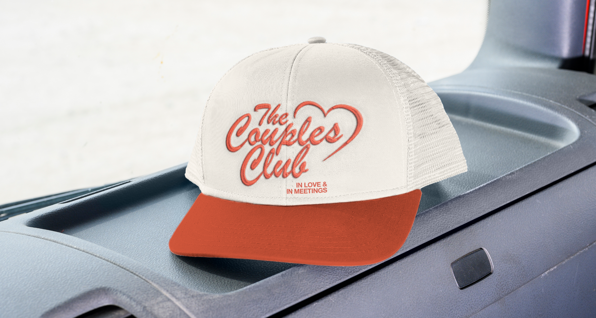 Truckers Cap with 'The Couples Club' text on a car dashboard