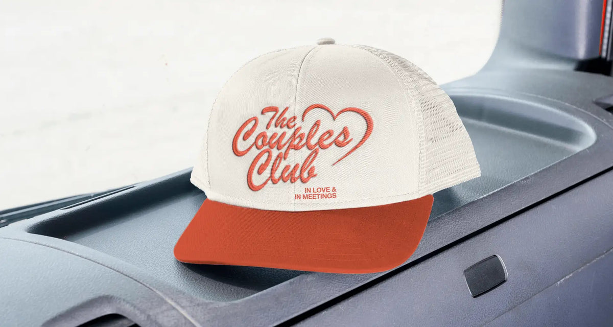 The Couples Club trucker hat design with heart script logo and “In love & in meetings” tagline