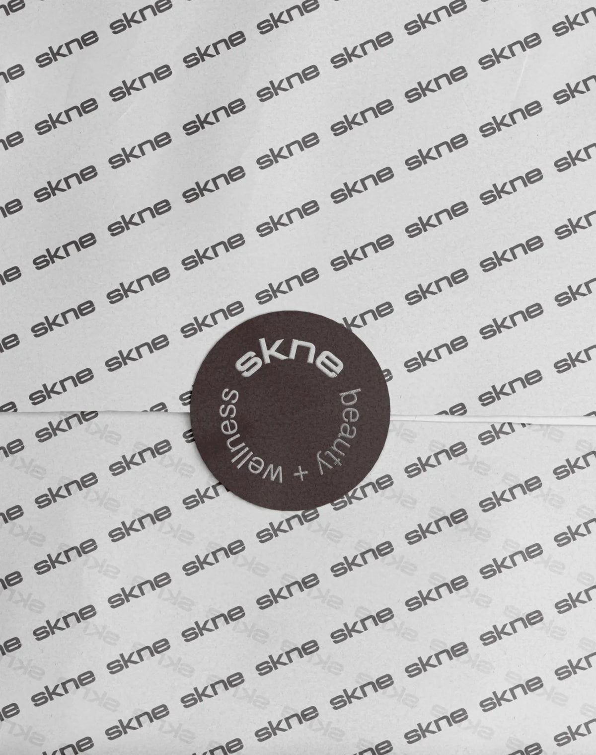 SKNE custom repeat-logo tissue paper with a circular “beauty + wellness” seal sticker