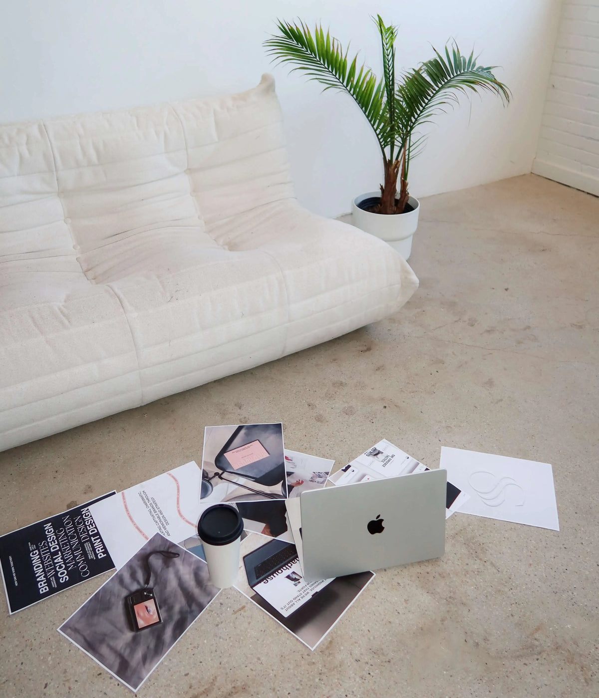 Laptop, coffee and printed branding and social media design work spread across the Madhouse Brands studio floor