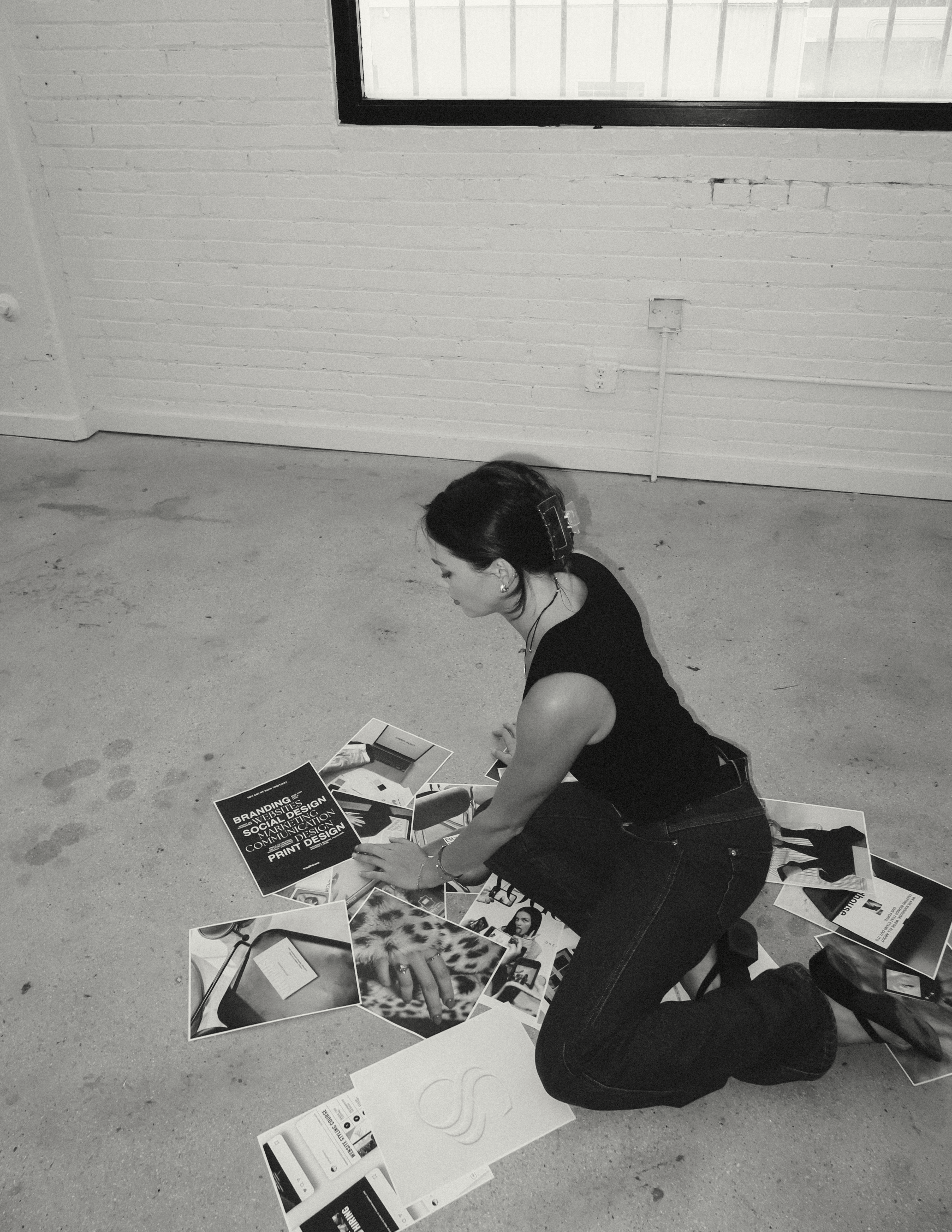 Madhouse Founder Madison Barnes sitting on the floor surrounded by brand images in a studio room with white walls and concrete floor.