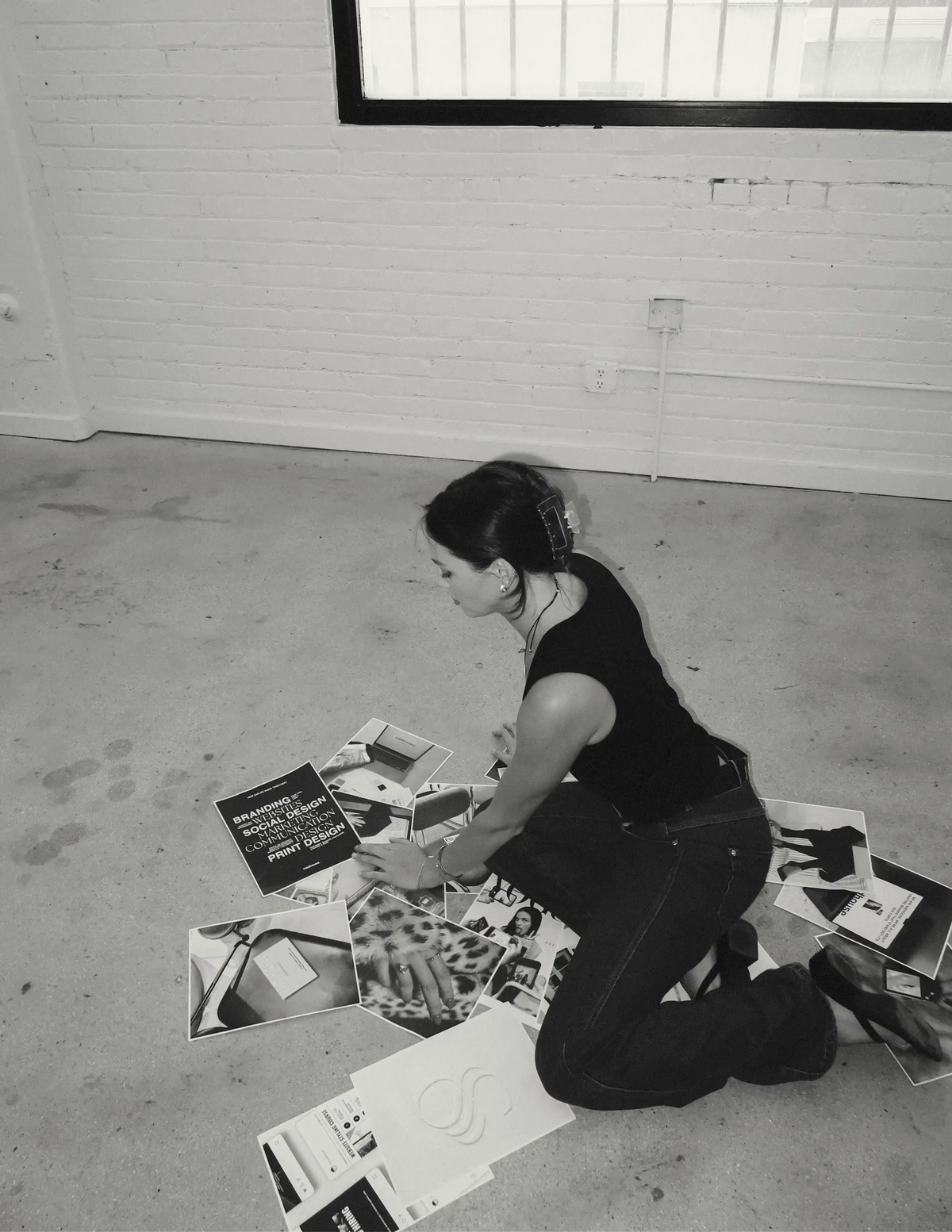 Madison Barnes, founder and designer of Madhouse Brands, arranging brand design prints on the studio floor (black and white)