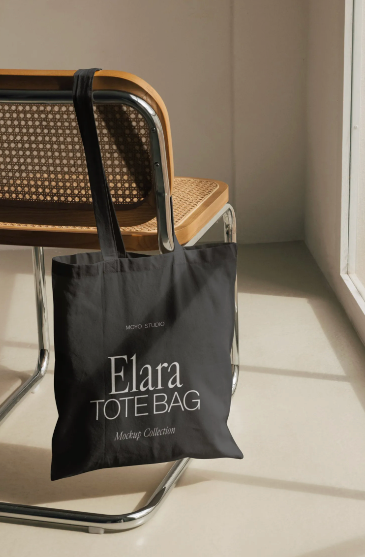 Moyo Studios Mockup - Black tote bag with 'Elara Tote Bag' text on a chair in a minimalistic setting
