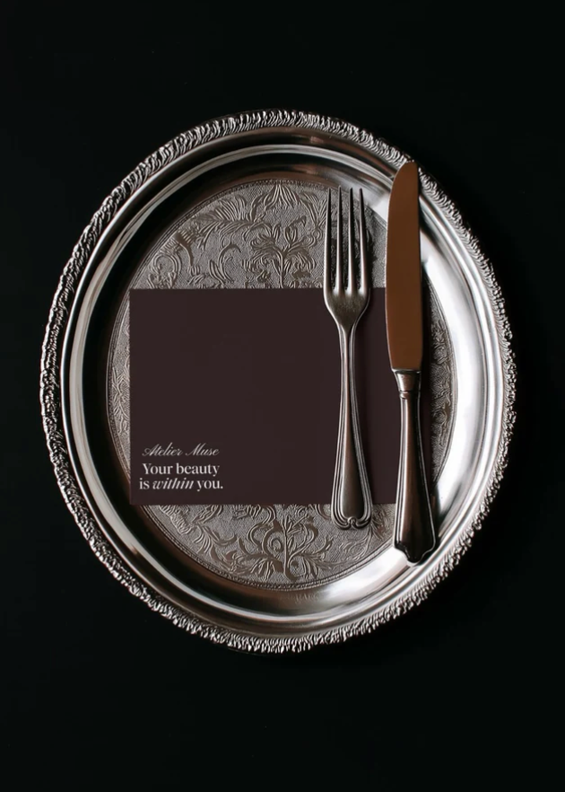 Studio Blanche Mockup - Silver platter with engraved design, black napkin, fork, and knife on a black background
