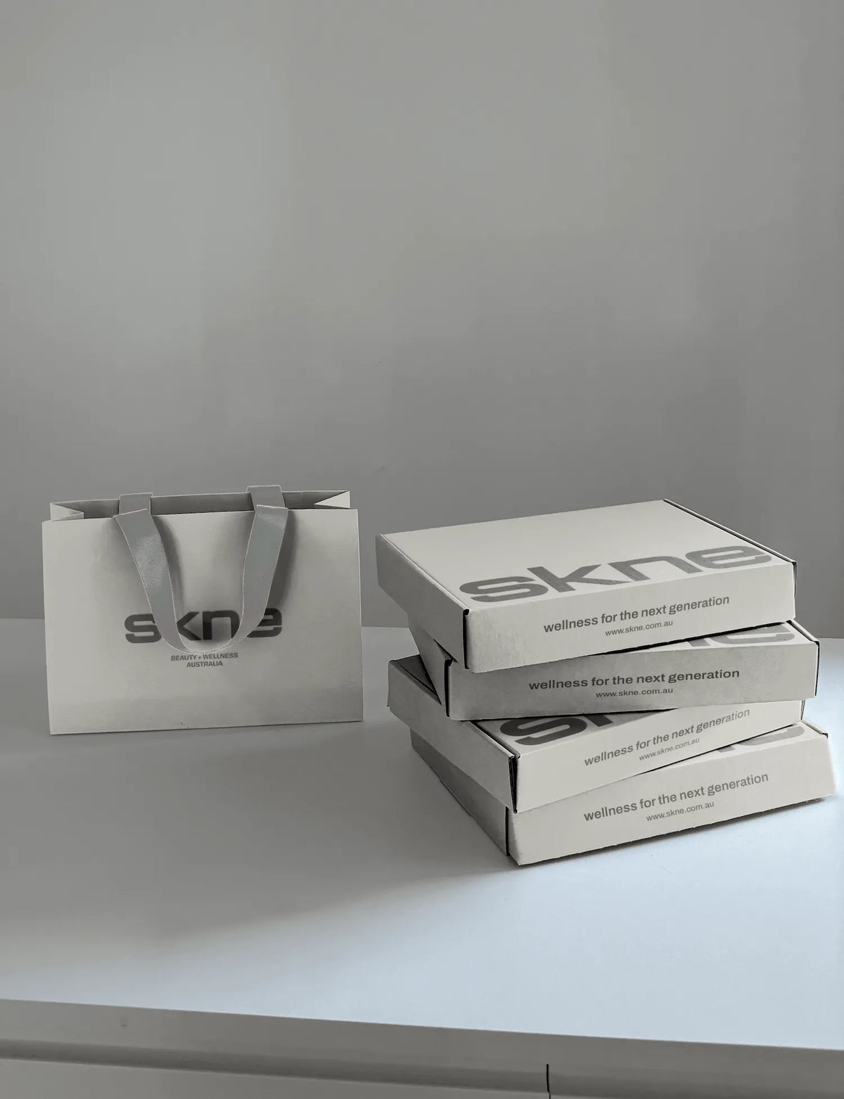 SKNE packaging design: branded shopping bag and stacked mailer boxes with “wellness for the next generation” tagline