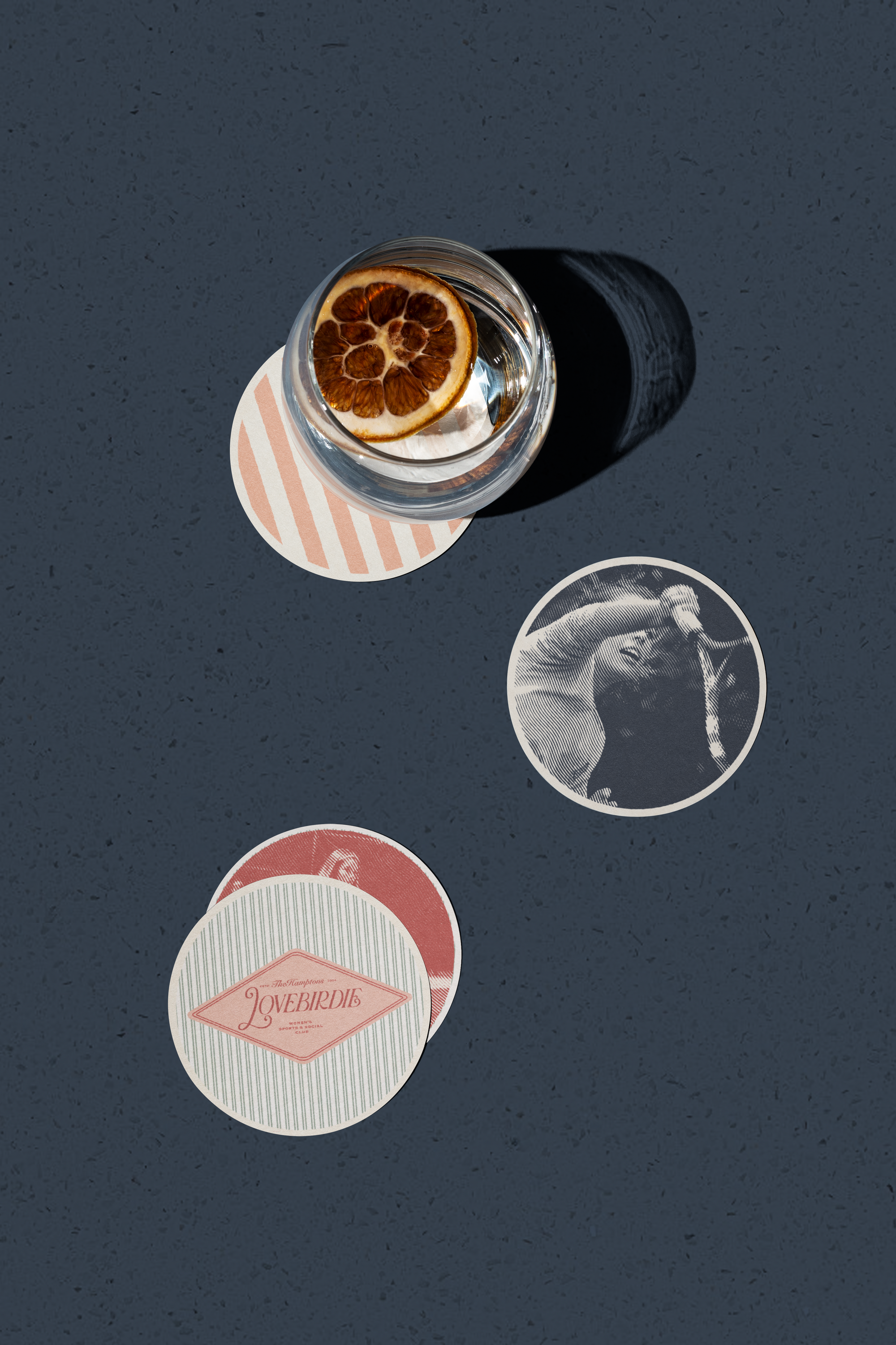 Glass with an orange slice garnish, coasters with branded designs.