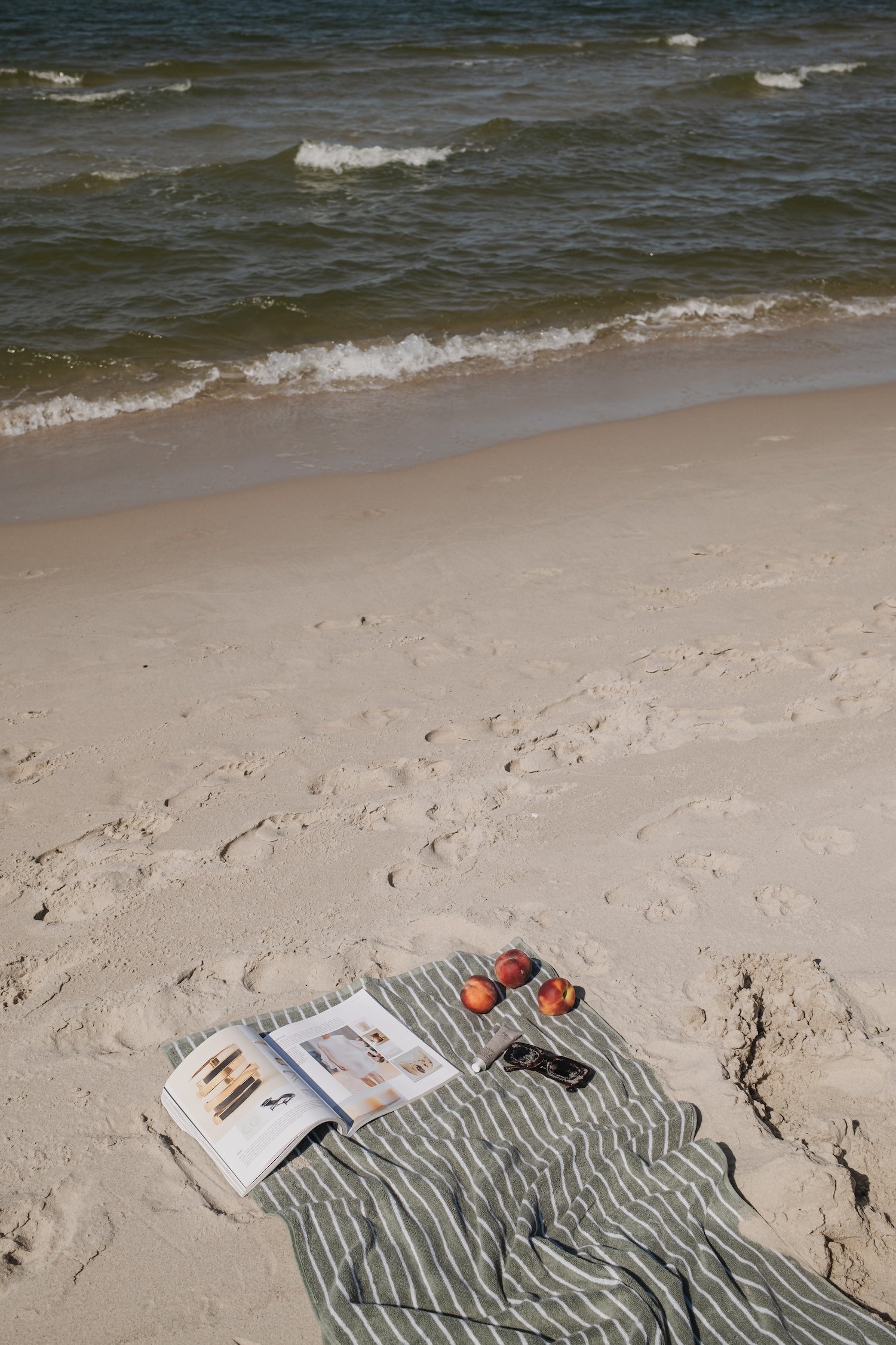 Open book and sunglasses on a striped towel at the beach with waves in the background